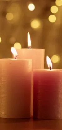 Decorate your phone screen with this soothing live wallpaper featuring three pink-lit candles sitting in a row on a table