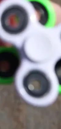 Get mesmerized by this lively and dynamic phone live wallpaper featuring a green and white fidget spinner spinning rapidly in extreme close-up