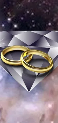 This stunning phone wallpaper showcases two gold wedding rings on top of a sparkling diamond, forming a luxurious and elegant image