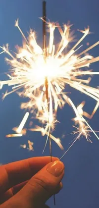 This stunning live phone wallpaper showcases a sparkling sparkler in a user's hand against a sunny background