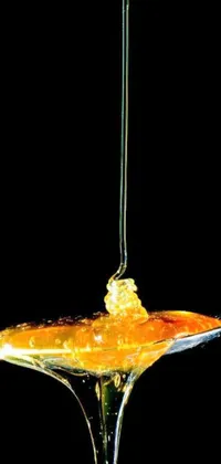 This live wallpaper features a digital rendering of a spoon with liquid made of honey, dripping from the ceiling against a black background