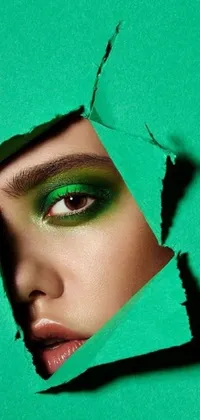 This live wallpaper for phones is a stunning work of art that features an eye-catching image of a woman peering through a hole in green paper