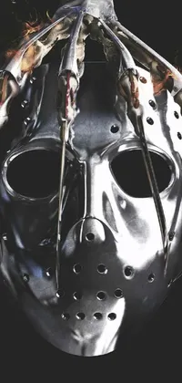 This phone live wallpaper features a metal mask with intricate details on a dark background, inspired by horror movies