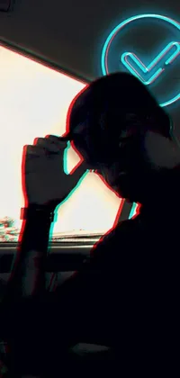 This dark and eye-catching live phone wallpaper showcases a mysterious man sitting in a car speaking on his mobile phone while wearing a black visor