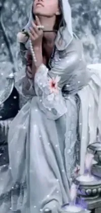 This live phone wallpaper showcases a colorized photo of a woman wearing silver robes sitting in the snow