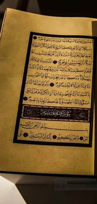 This phone live wallpaper presents an open book on a table with intricate hurufiyya writing
