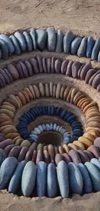 Get lost in the unique beauty of this live phone wallpaper featuring a captivating spiral made of stones in the sand