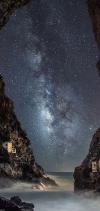This phone live wallpaper showcases the stunning Milky Way galaxy as seen from inside a cave with a small village in the foreground