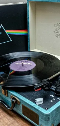 This phone live wallpaper features a blue suitcase resting on a wooden table with a vinyl record album cover featuring holographic designs nestled beside it