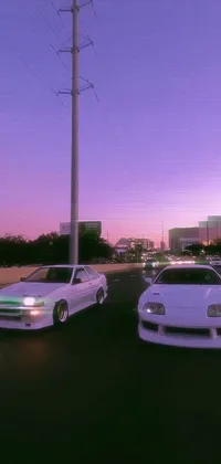 This live phone wallpaper displays two white cars driving down a street at sunset, featuring a realistic scene with Y2K aesthetics and a Toyota Supra