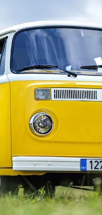 This phone live wallpaper showcases a beautiful vintage yellow Volkswagen bus parked in a lush green field