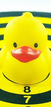This live phone wallpaper features a vibrant yellow rubber duck resting on a dart, amid a colorful op art background