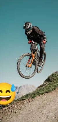 This thrilling phone live wallpaper features an exciting image of a daredevil biker soaring through the air against a scenic mountain backdrop