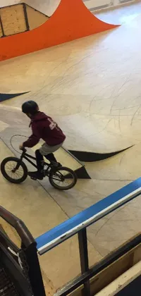 Looking for an action-packed live wallpaper for your phone? Look no further than this thrilling indoor scene featuring a boy riding his bike on a ramp! The birdseye view provides a panoramic perspective, while the absence of extra ears or sounds makes for a simple yet exciting visual