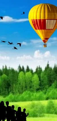 This mobile wallpaper depicts a charming scene of people admiring a hot air balloon set against a forest backdrop
