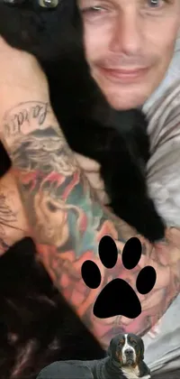 This phone live wallpaper features a man holding a black cat and a dog with a tattooed arm