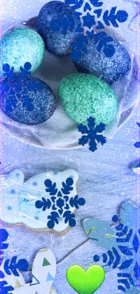 This lively phone wallpaper showcases a white plate bearing blue and green decorated cookies with a golden-bordered picture in the center, offering an elegant winter vibe