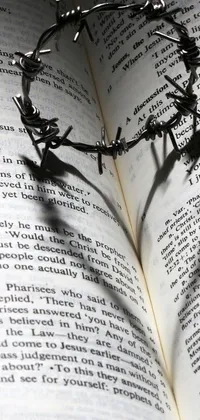 This stunning phone live wallpaper showcases a crown of barbed wire sitting atop an open book with a picture of a shadowy cross