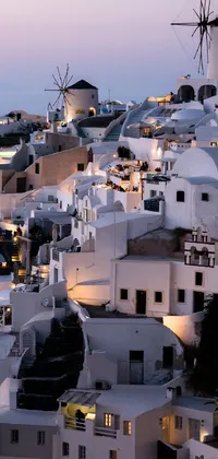 This live wallpaper depicts a scenic view of a white neoclassical building complex set atop a hill, accentuated by warm, inviting lights emitting from the windows, and Greek fabrics adorning some of the surfaces
