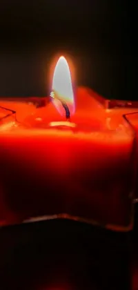 This phone live wallpaper features a red candle on a table with a white flame against a black background