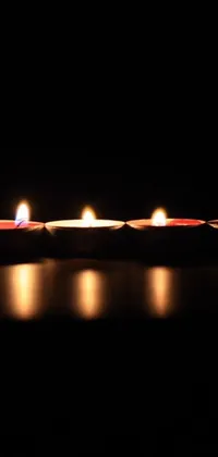 This elegant phone live wallpaper features a row of lit candles sitting on a table against a black background