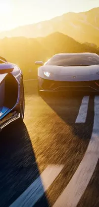 Looking for a dynamic live wallpaper for your phone? Look no further than this thrilling sports car wallpaper! Enjoy the sight of two powerful cars driving down a scenic mountain road, with sunlight illuminating every detail