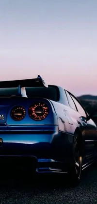 This live wallpaper features a modified blue Nissan Skyline R34 parked on the side of the road against a beautiful, sunset backdrop
