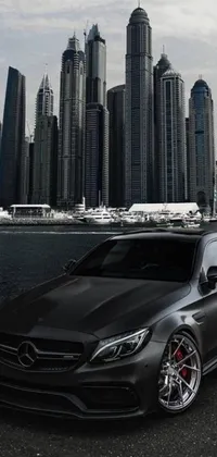 Elevate the look of your phone's background with this exquisite live wallpaper featuring a Mercedez Benz parked by the waterfront of a modern city