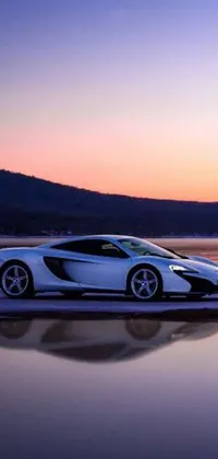 This stunning phone live wallpaper features a white sports car parked on a beach at sunset with a mountain in the background and a body of water in the foreground