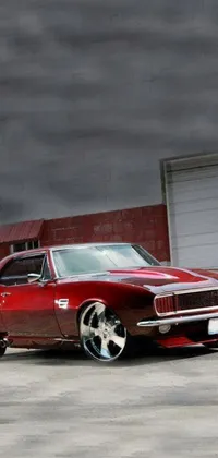 This phone live wallpaper features a highly-detailed digital rendering of a classic red muscle car parked in front of a garage