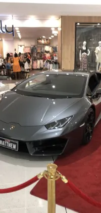 This live wallpaper depicts a silver Lamborghini parked on a red carpet in a black showroom within a mall