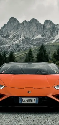 Get a captivating phone live wallpaper featuring an orange sports car in front of a beautiful mountain range