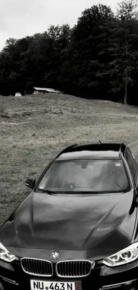 This phone live wallpaper features a black BMW parked on the side of a dirt road in a farm