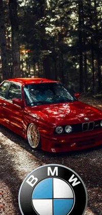 This phone live wallpaper showcases an eye-catching red BMW car parked amidst a scenic forest