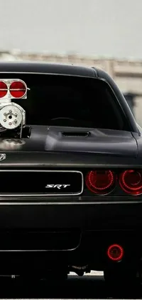 This dynamic phone live wallpaper features a black car with a red tail light and a white clock on its hood as it speeds down a winding road in the moonlight