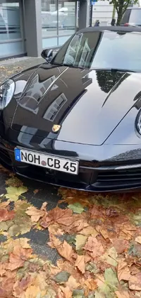 This live wallpaper showcases a highly detailed frontal angle of a sleek black sports car parked on the side of a quiet road, surrounded by beautiful autumn scenery