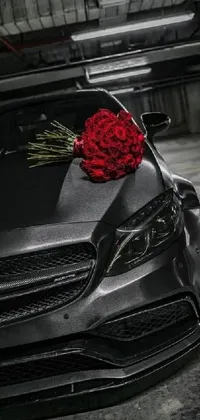 This live wallpaper showcases a stylish Mercedes car painted in a sleek gunmetal grey color, with a beautiful bunch of red roses on the hood
