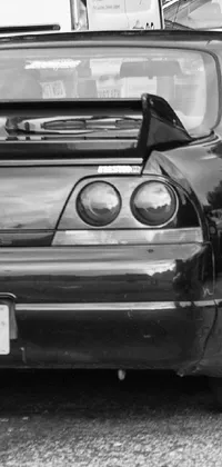 This live wallpaper for your phone showcases a striking black and white photograph of a modified Nissan Skyline R34 parked in a lot