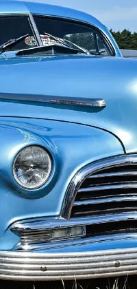 This live phone wallpaper depicts a blue vintage car parked on a lush green field