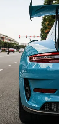 Admire the beauty of a stunning light blue Porsche sports car parked on the side of the road with this phone live wallpaper