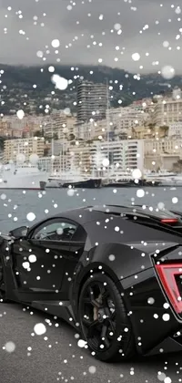 This phone live wallpaper depicts a sleek black sports car parked alongside a tranquil body of water with a stunning background