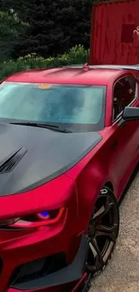 This red Chevrolet Camaro phone live wallpaper features a parked car in front of a truck with a gradient red to black brushed rose gold car paint, dynamic headlights and taillights, smoke coming out of the exhaust pipe and a subtle revving engine sound
