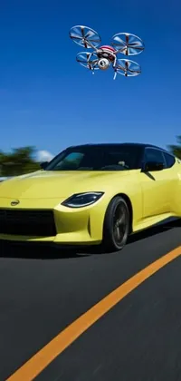 This phone live wallpaper features a bright yellow sports car driving down a scenic road surrounded by greenery