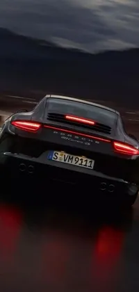 Get ready to enhance your phone display with this stunning sports car live wallpaper! The image features a sleek black Porsche 911 driving down a dimly lit road at night, with the car's back view beautifully highlighted against the background's subdued lighting