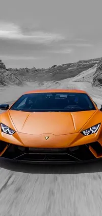 This live phone wallpaper showcases an orange Lamborghini sports car driving on a desert road