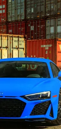 Enhance your phone display with our thrilling live wallpaper! Featuring a blue sports car parked in front of colossal shipping containers and an op art technique, this portrait is sure to captivate your attention