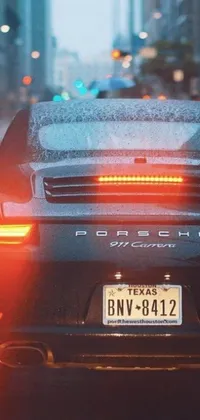 This phone live wallpaper depicts a black Porsche 911 in the future engine design driving down a city street in evening rain