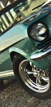 This phone live wallpaper displays a vintage green classic car on a cobblestone street