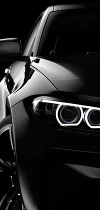 This phone live wallpaper features a close up of a sleek black BMW with its headlights on, set against an elegant white and black background