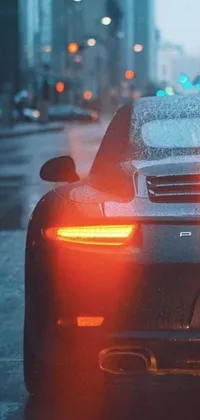 This phone live wallpaper features a close-up view of a luxurious Porsche parked on a city street during an evening rain